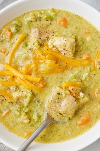 Creamy chicken broccoli soup in a bowl with a spoon, lifting up a bite.