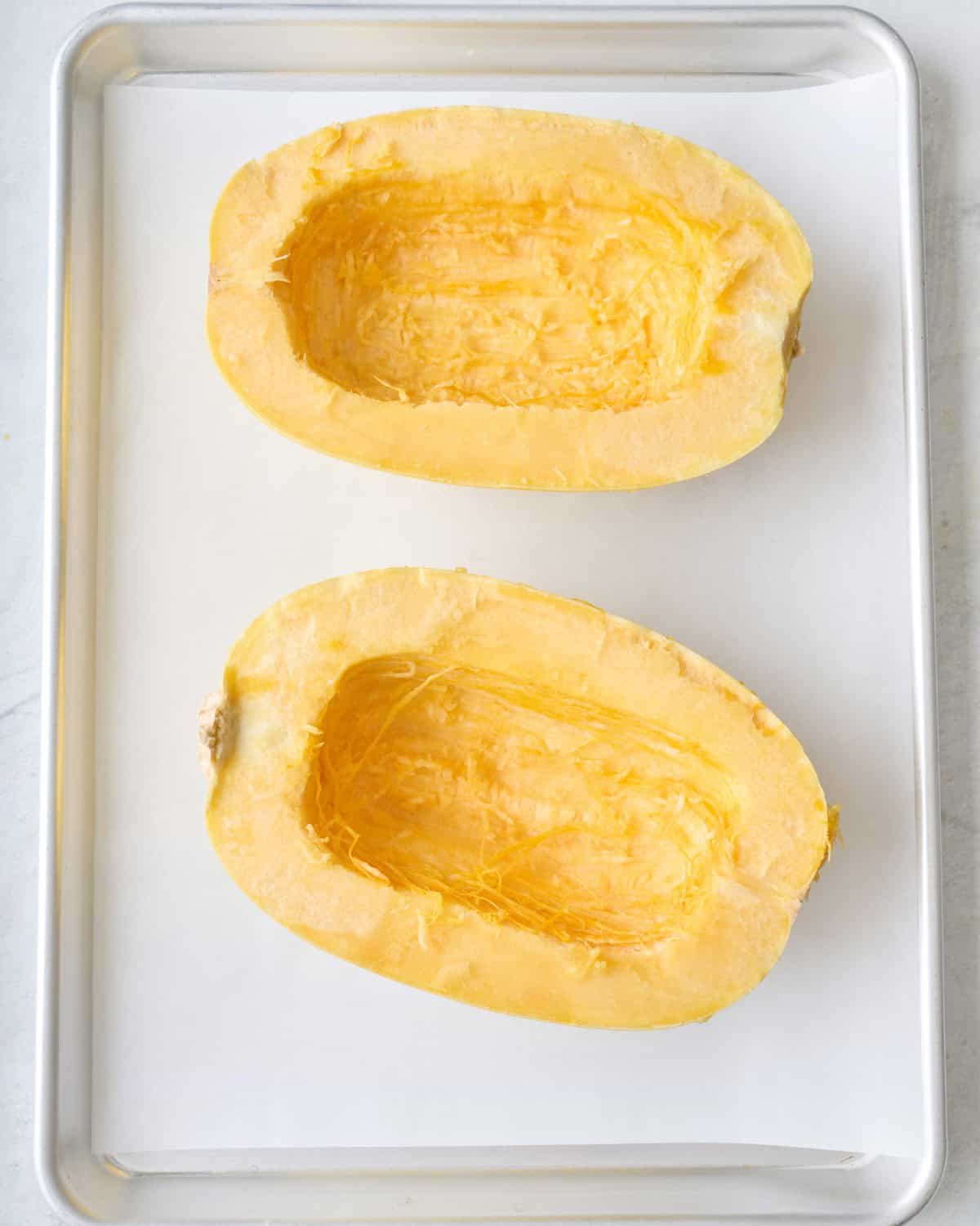 Two prepared spaghetti squash halves cut, side up on a sheet pan.