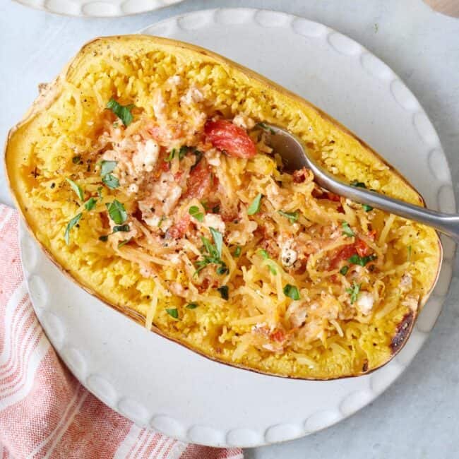 A fork scooping from a feta spaghetti squash made with cherry tomatoes and garlic on a white round plate.