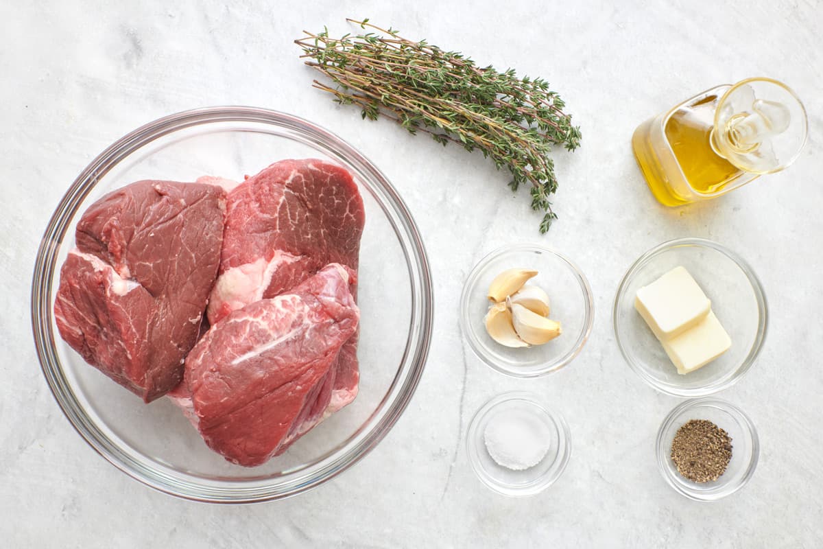 Ingredients for recipe before prepping: 4 cuts of filet mignon, fresh thyme, garlic cloves, salt, oil, butter, and pepper.