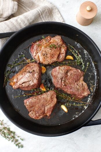 Filet mignon cooked in a cast iron skillet with butter, garlic, and fresh thyme.