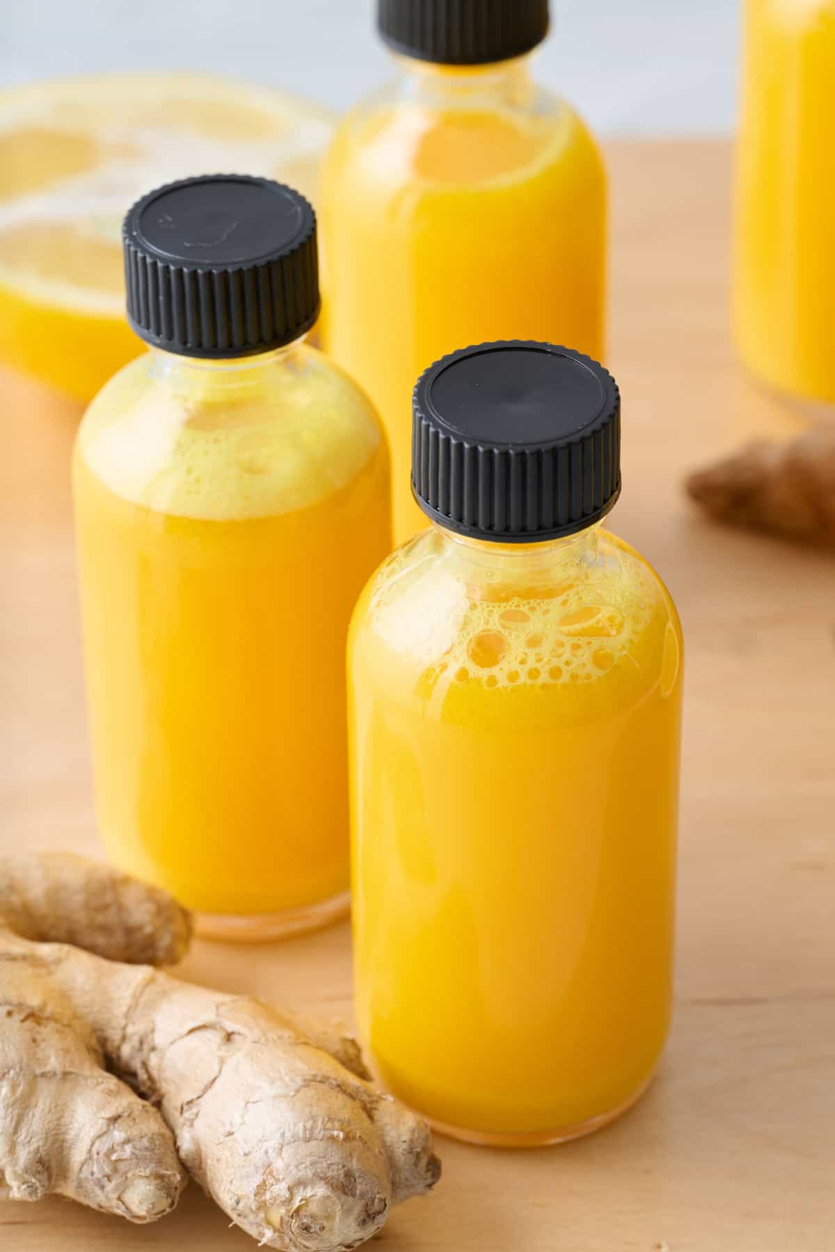 Close-up of ginger shots in small glass bottles with ginger nearby.