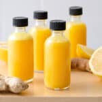 Ginger shots in small glass bottles with ginger roots and lemons nearby.