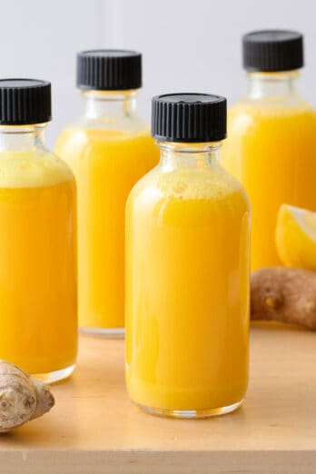 Ginger shots in small glass bottles with ginger roots and lemons nearby.