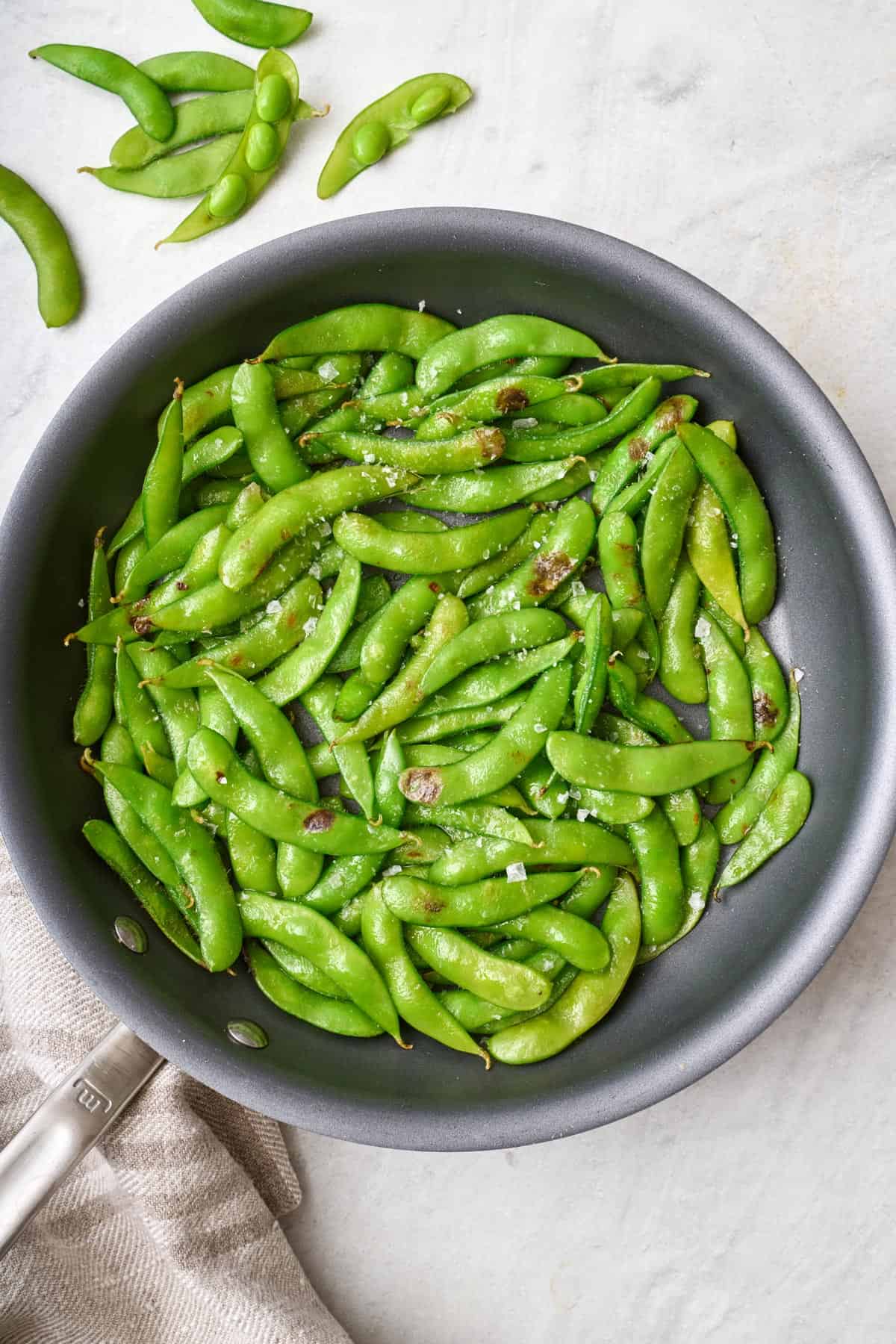 Pan-seared whole edamame pods in a skillet, garnished with flaky sea salt.