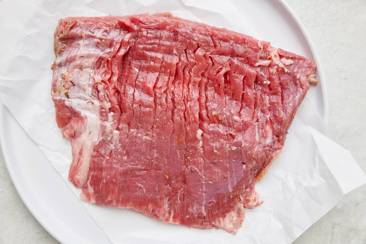 Flank steak on a piece of parchment paper before cooking.