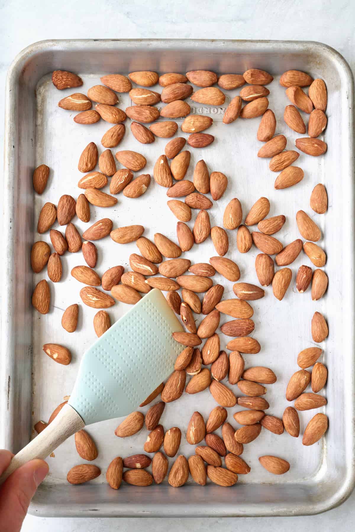 Toasted whole almonds on a baking sheet with a spatula pushing some around.