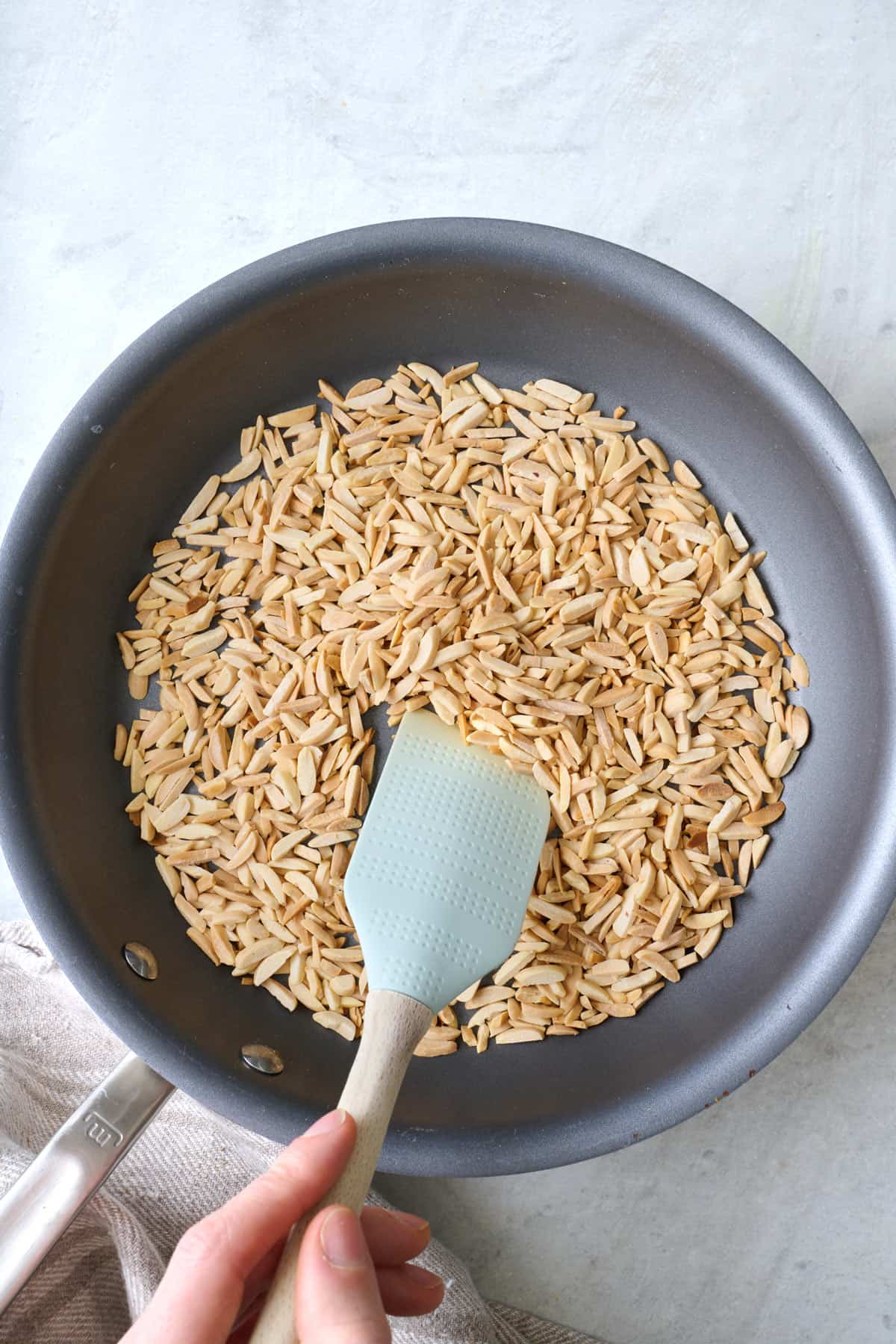 Toasted slivered almonds in a skillet with a spatula pushing them around.