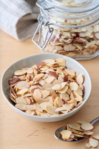 Toasted sliced almonds in a bowl with a small jar of more nearby.