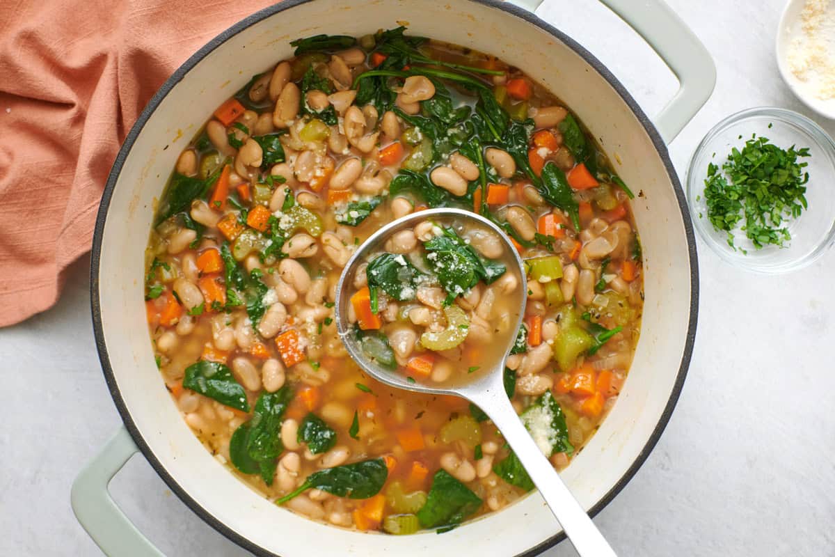 A pot of white bean soup with a ladle holding up some. 