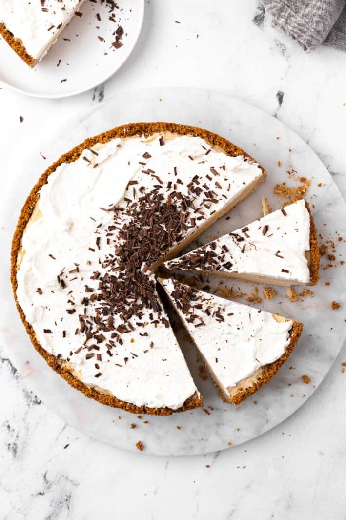 No-bake peanut butter pie with shaved chocolate sprinkled on it, cut into slices, sitting on marble with a slice nearby on a small plate.