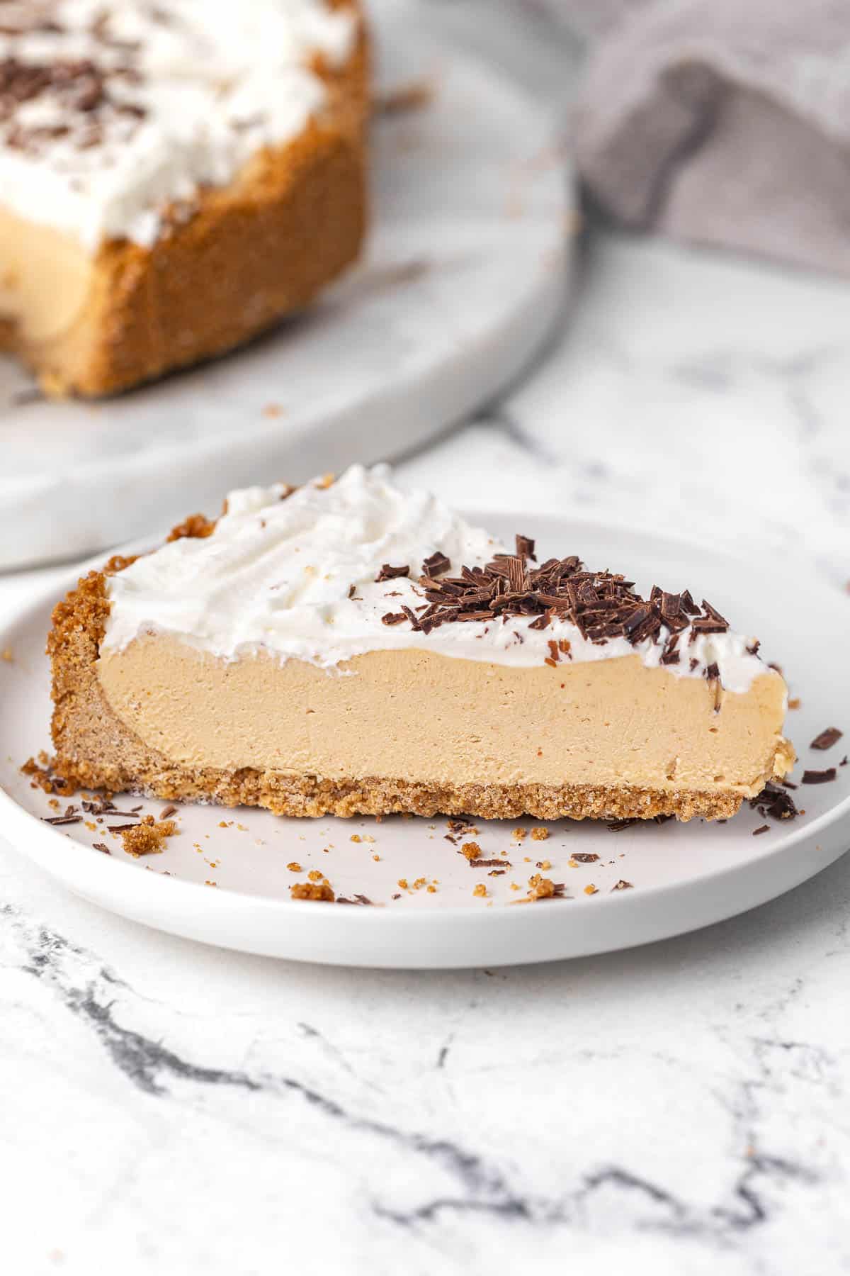 A close-up of a slice of no-bake peanut butter pie on a white round plate.