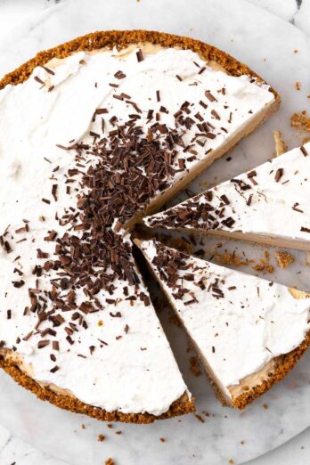No-bake peanut butter pie with shaved chocolate sprinkled on it, cut into slices, sitting on marble.