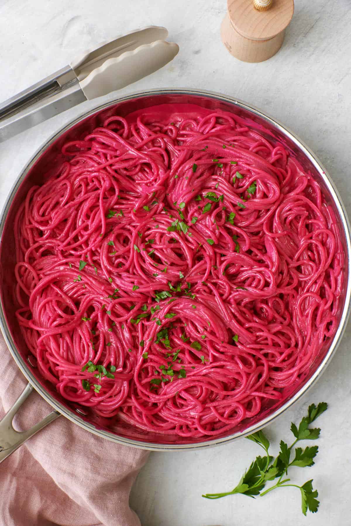 Pink beet pasta in a skillet garnished with fresh chopped parsley.