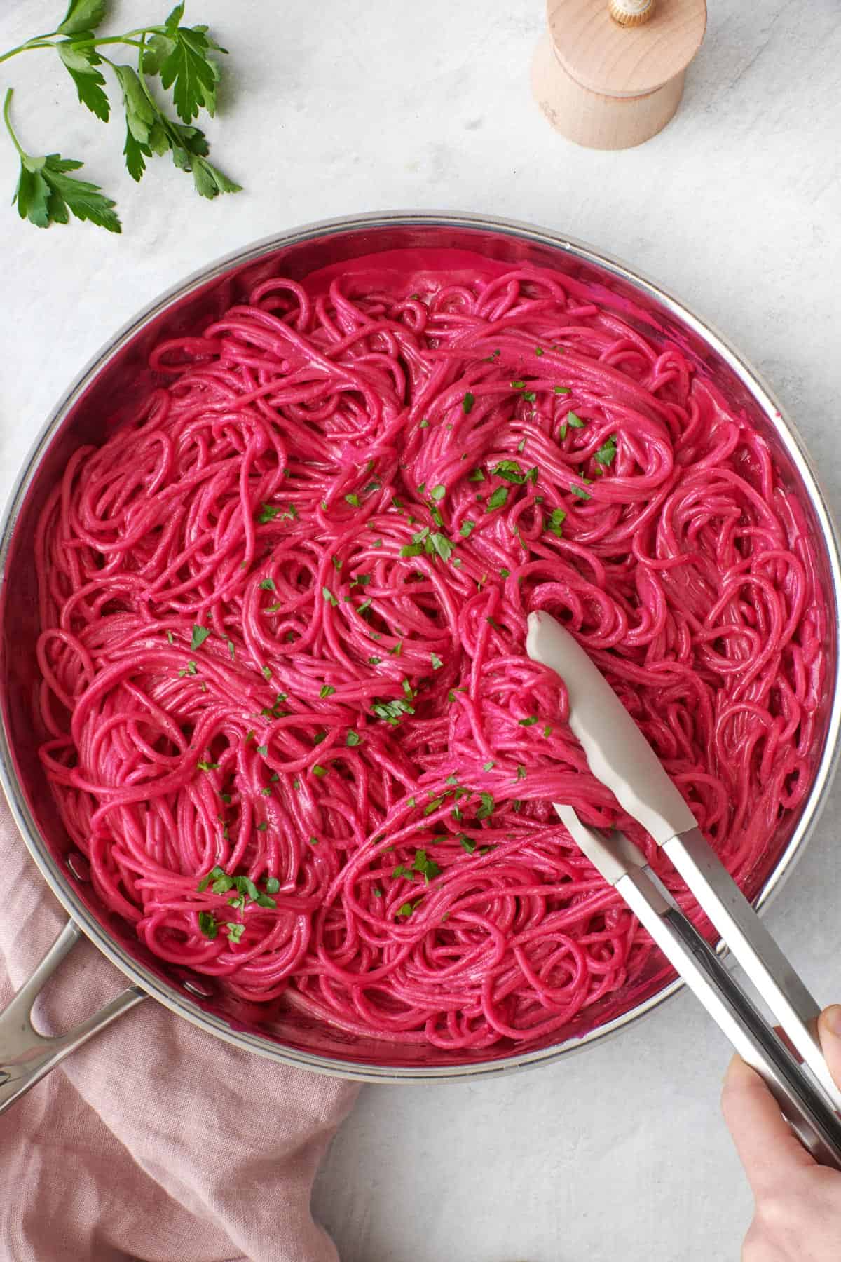 Pink pasta in a skillet with tongs lifting some up, garnished with fresh parsley.