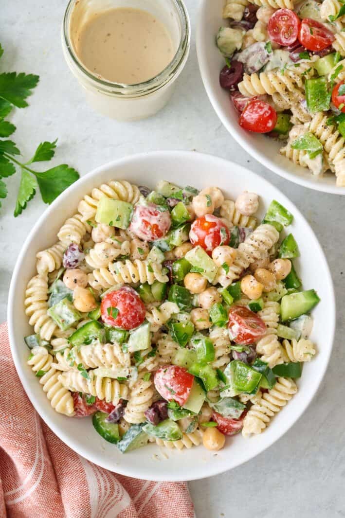 Overhead of a small bowl of tahini pasta salad with dressing and a serving bowl of the salad nearby.