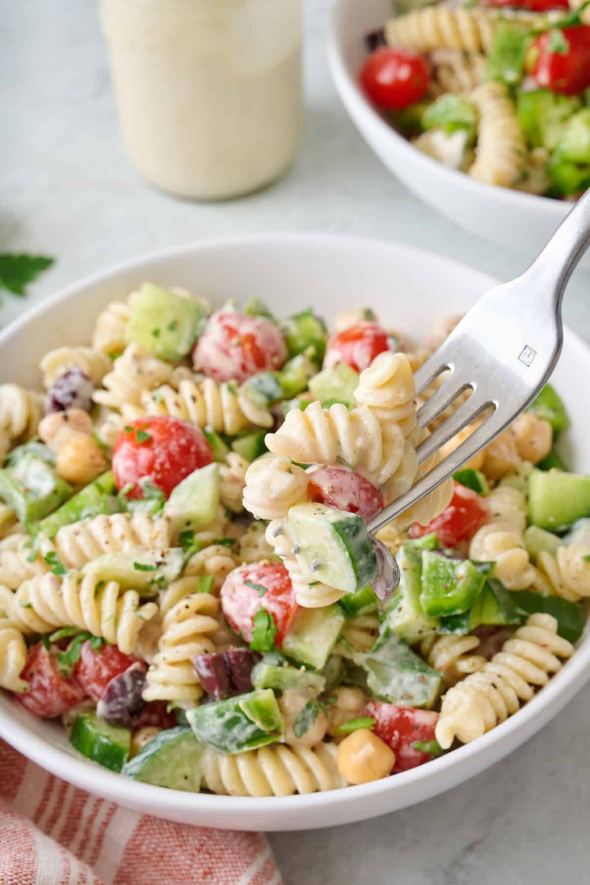 A fork scooping up a bite of tahini pasta salad from a small bowl.