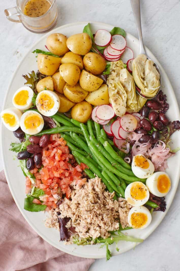 Tuna Nicoise Salad on a large oval platter with dressing nearby and a serving spoon on the plate.