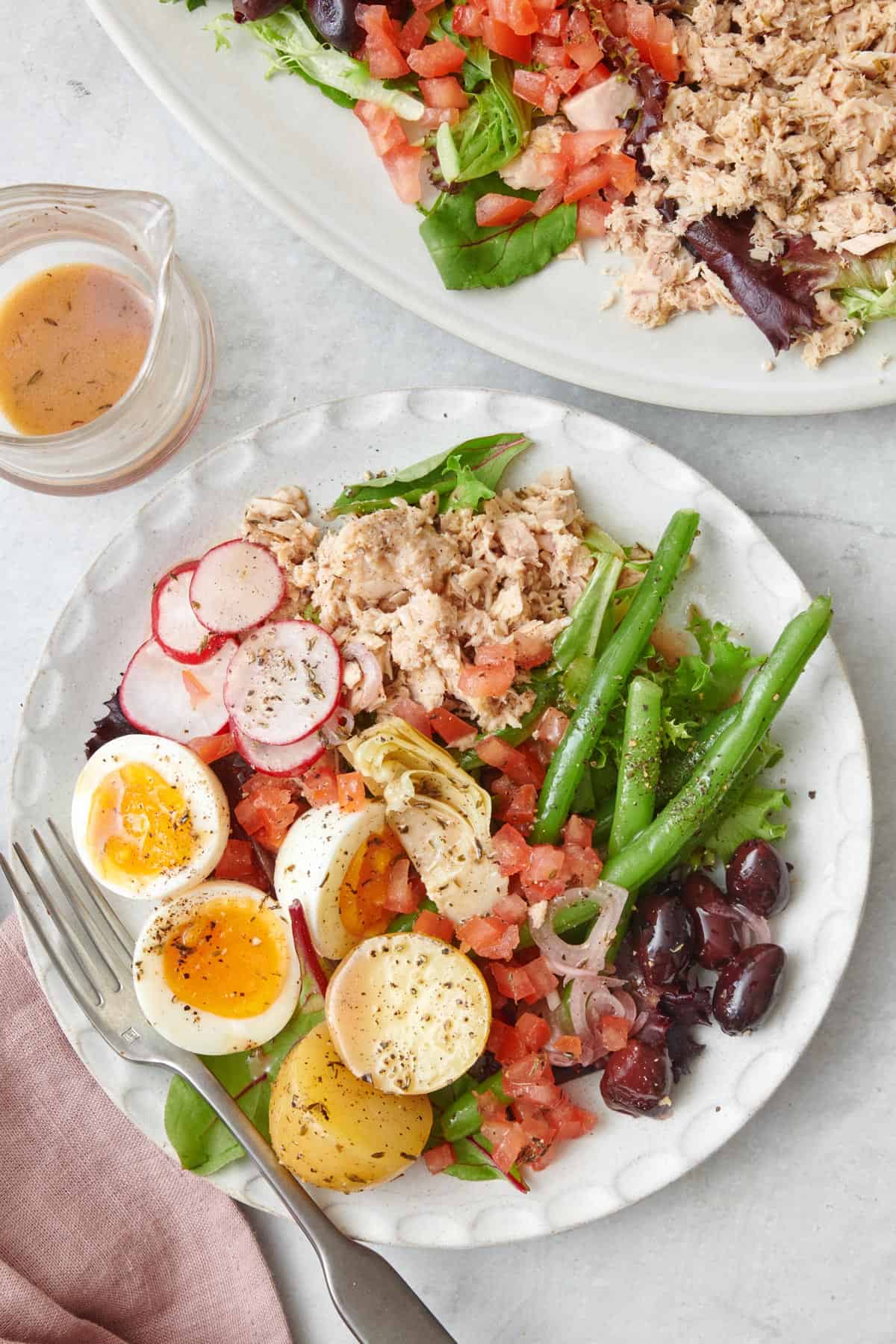 Serving of tuna nicoise salad on a small plate with serving platter nearby.