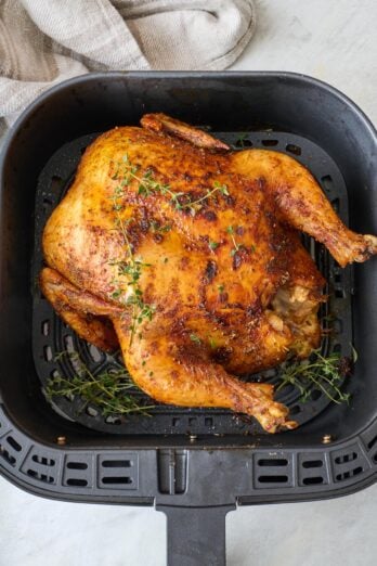 Air fryer whole chicken in air fryer after being cooked; garnished with fresh thyme.