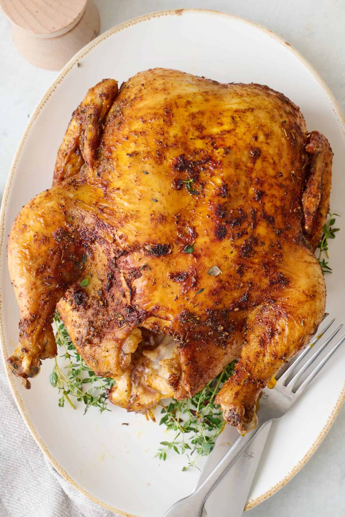 Air fryer whole chicken on serving platter with carving knife and fork.