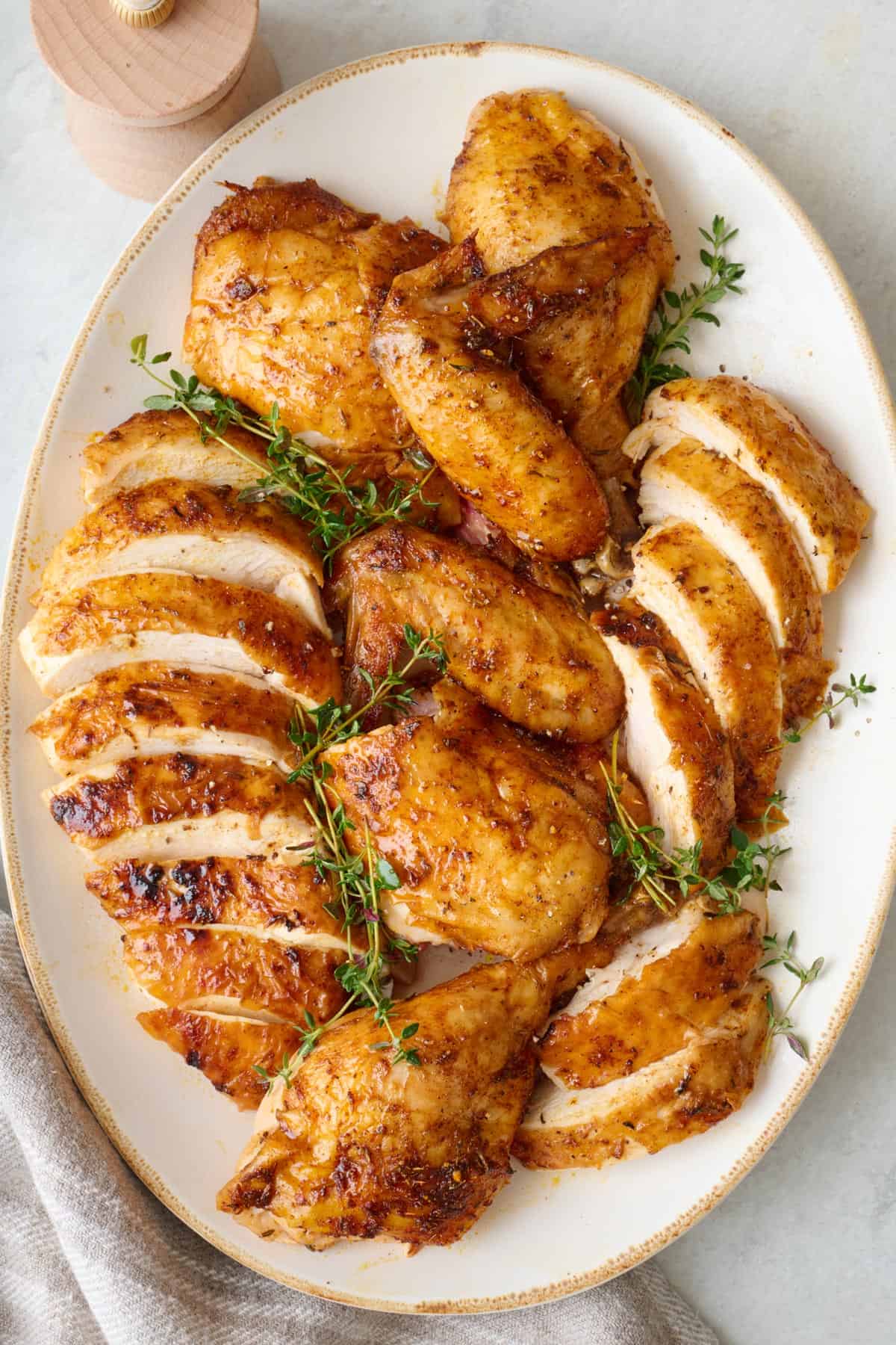 Air fryer whole chicken on a platter after cut into sliced breasts and whole legs, thighs, and wings; garnished with fresh thyme.
