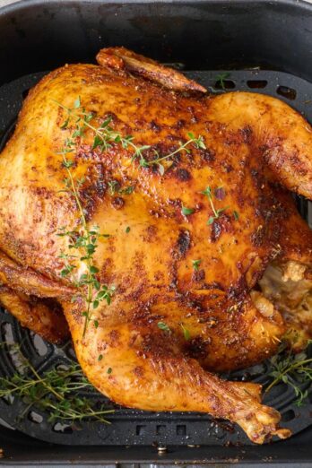 Whole chicken in air fryer after cooking, garnished with fresh thyme.