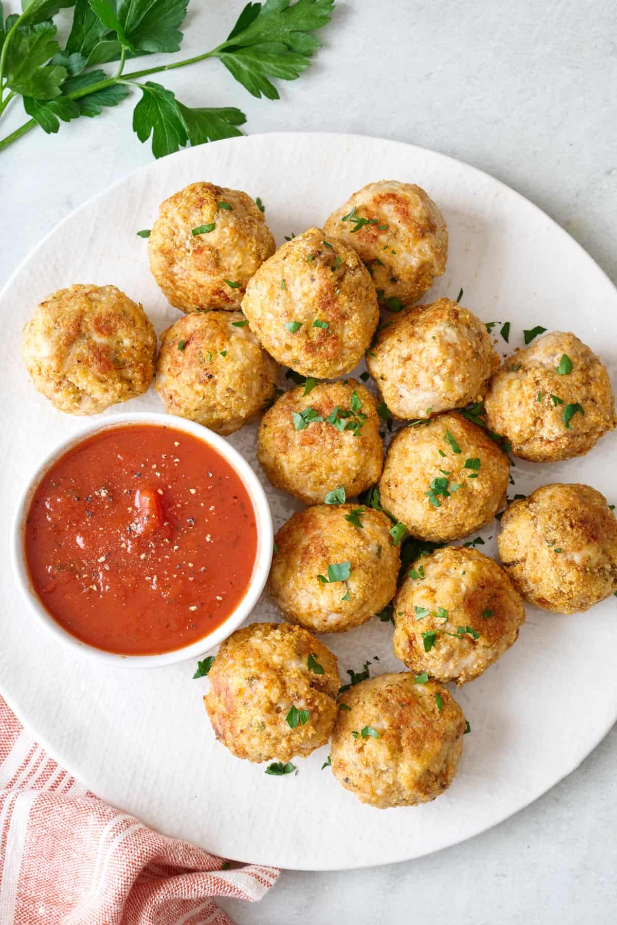 Plate of parmesan baked chicken meatballs with a side of marinara sauce for dipping.