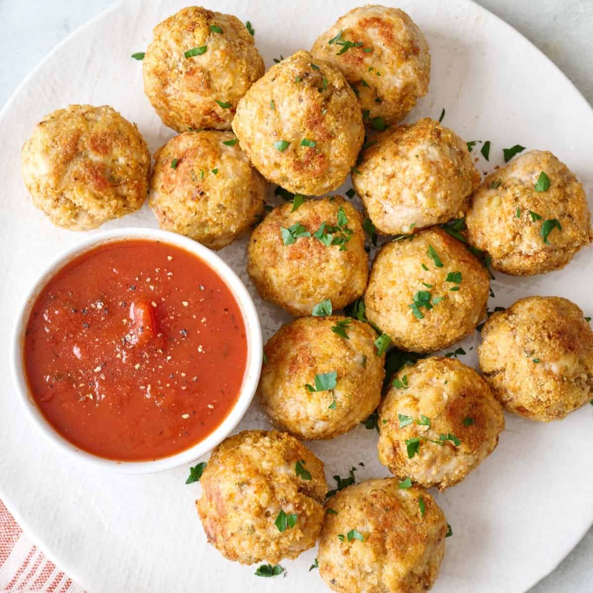 Baked chicken meatballs on a plate with a side of marinara sauce.