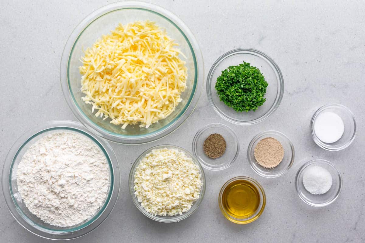 Ingredients for recipe before prepping: cheese, flour, feta, chopped parsley, black pepper, oil, instant yeast, sugar, and salt.