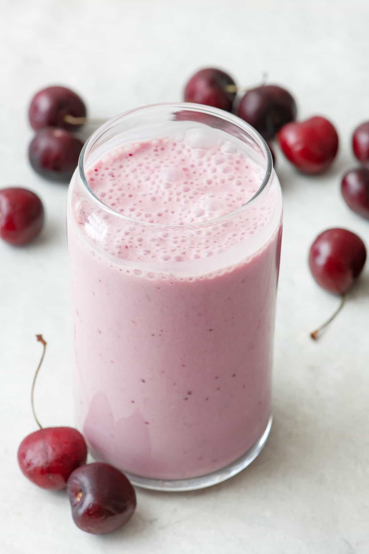 Glass of cherry smoothie surrounded by cherries.