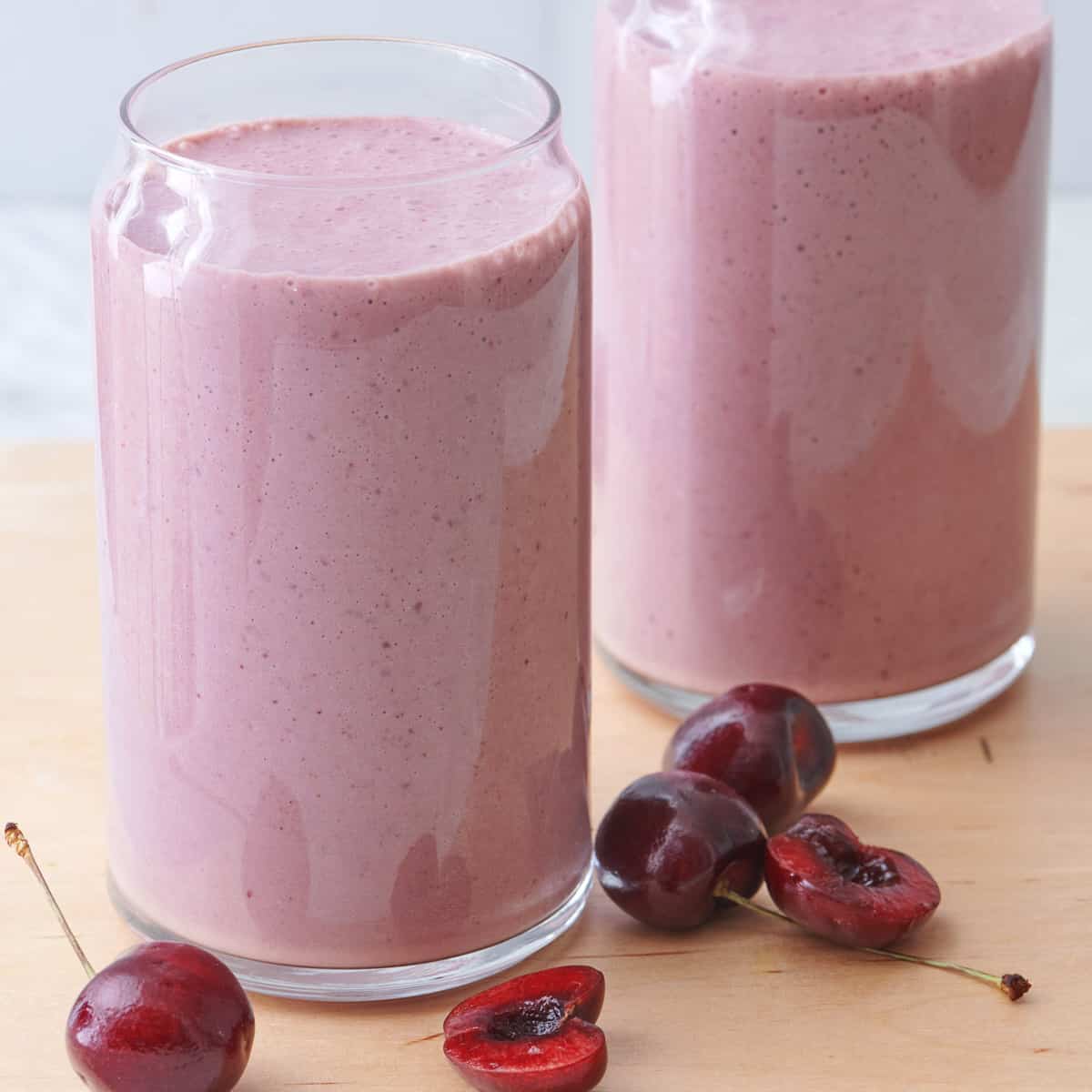 2 glasses of cherry smoothie with cherries surrounding them.