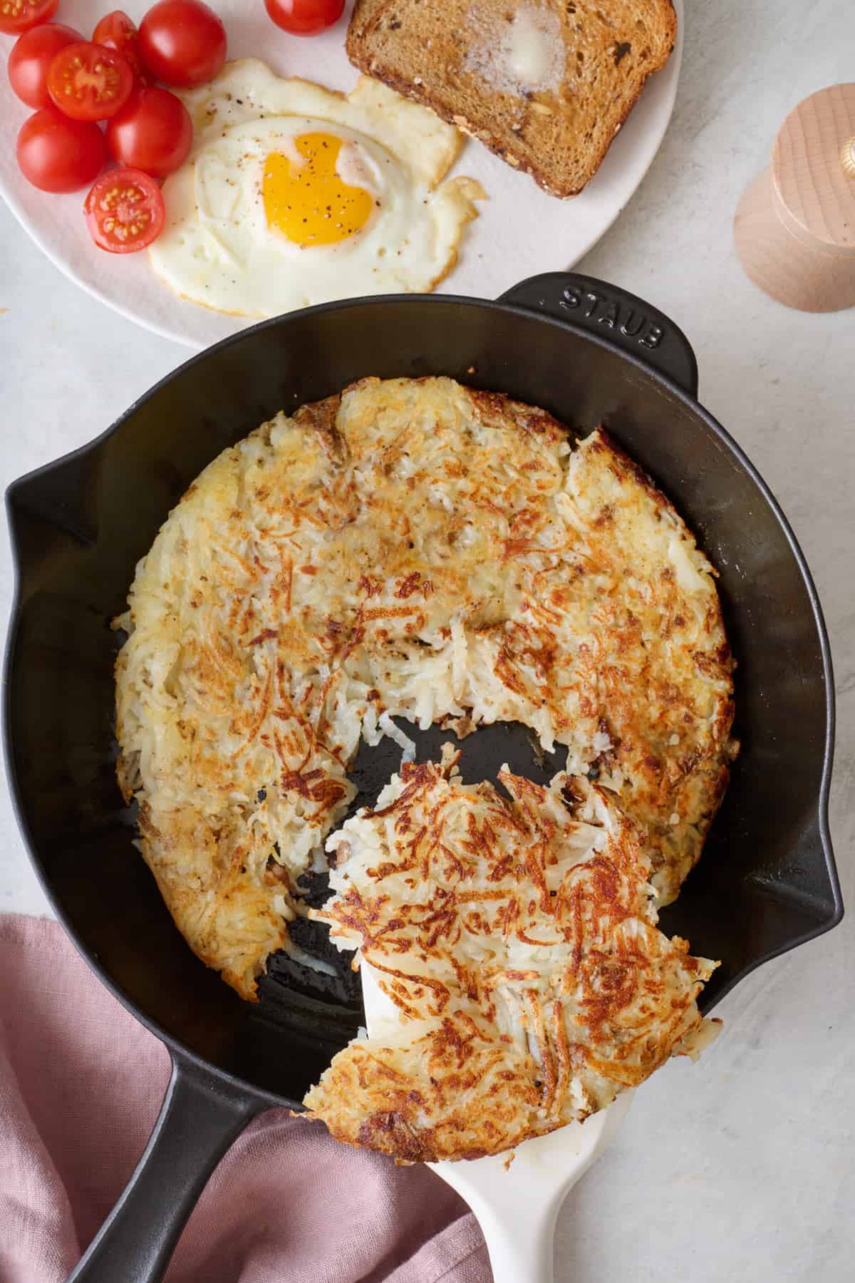 Spatula scooping out a serving of crispy hash browns from a skillet.