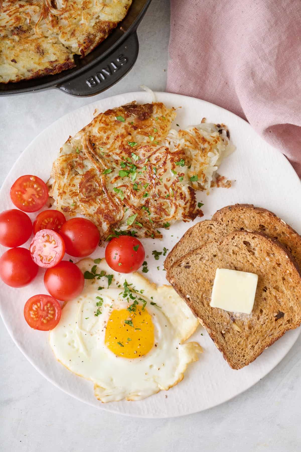 Crispy hash browns on a plate with cherry tomatoes, toast with butter, and a fried egg.