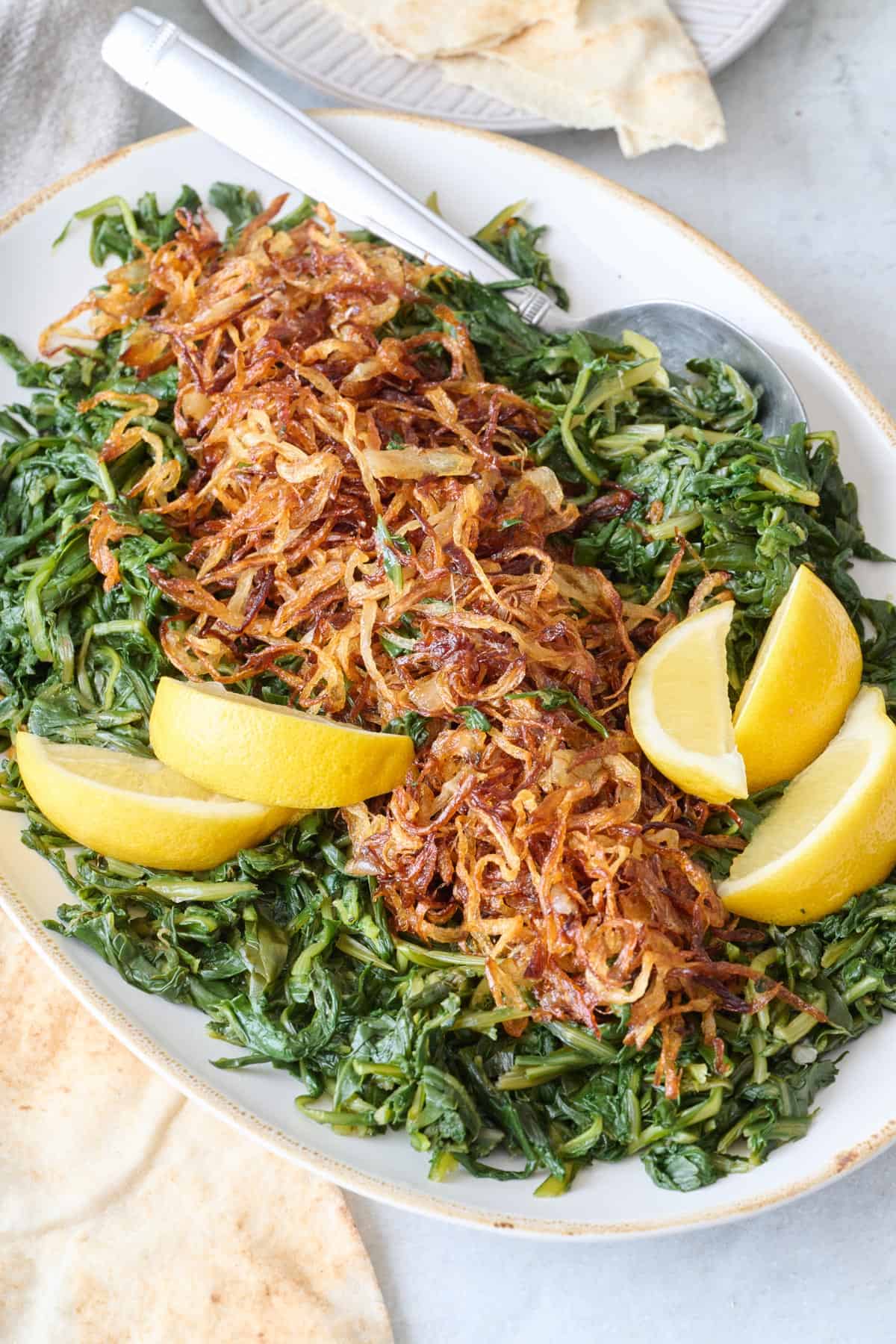 Platter full of cooked dandelion greens with crispy onions and lemon wedges.