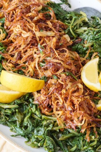 Dandelion greens with crispy fried onions on top, garnished with lemon wedges.