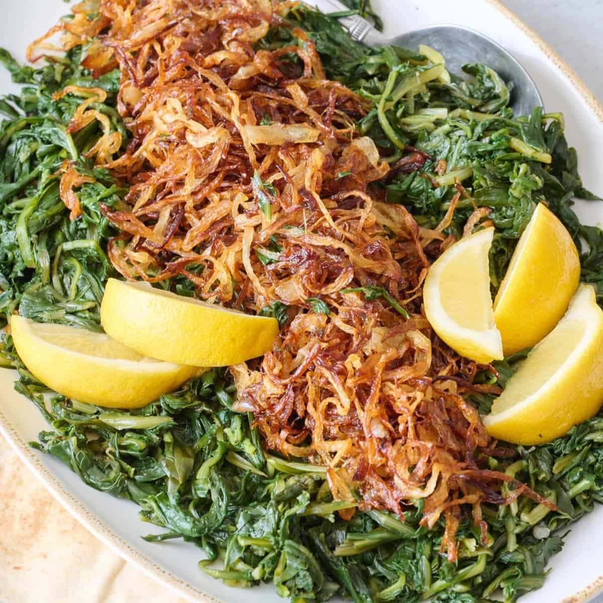 Dandelion greens with crispy fried onions on top, garnished with lemon wedges.