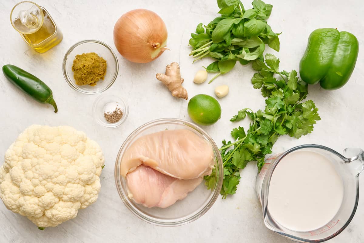 Ingredients for recipe before prepping: oil, jalepeno, cauliflower, green curry, salt and pepper, onion, ginger, chicken breasts, lime, garlic cloves, cilantro, basil, and green pepper.
