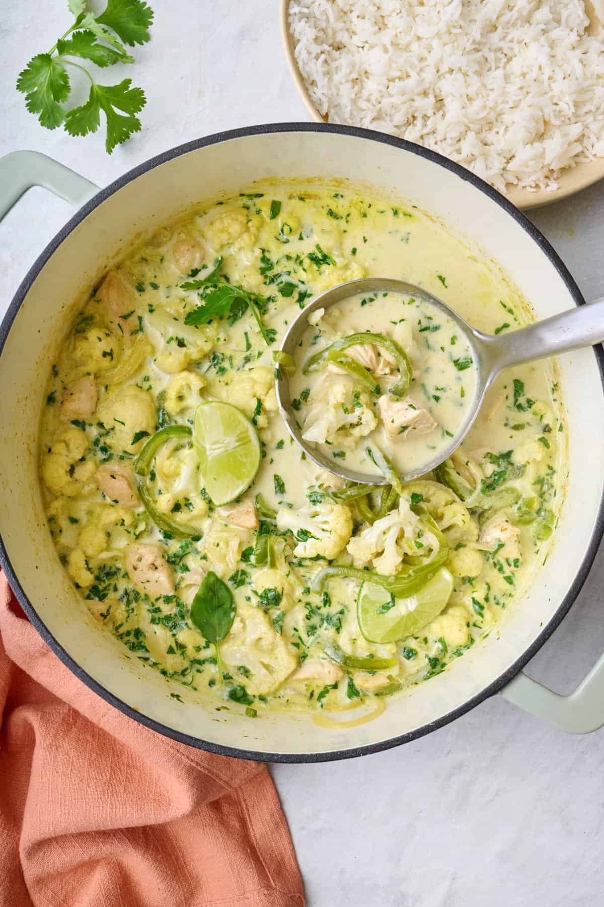 Green thai curry chicken in a pot with a ladle lifting some up.