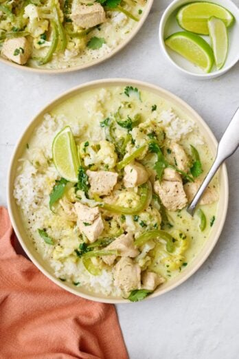 Green Thai curry with chicken served over rice in a bowl with a spoon dipper in.