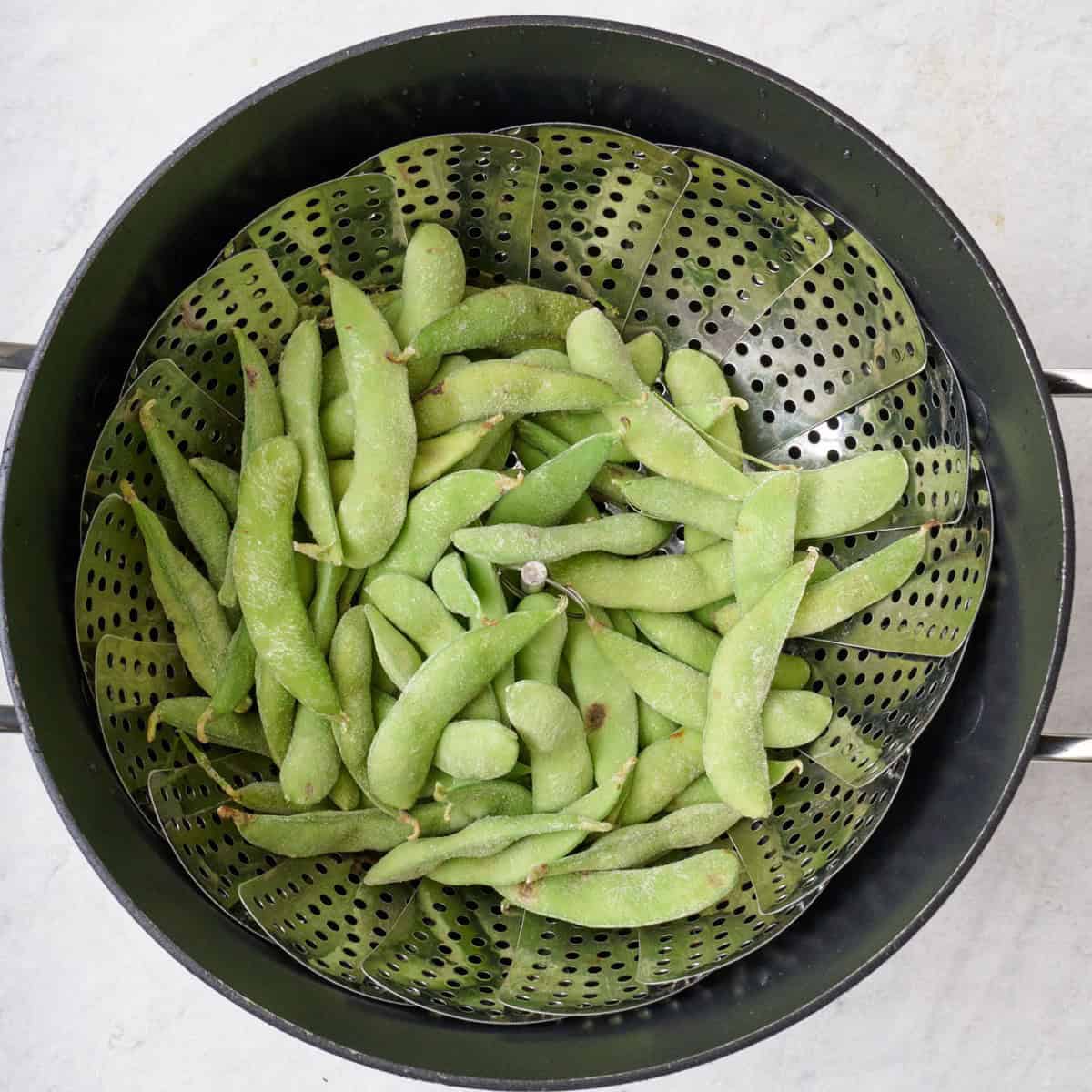 Edamame in a steam basket over a pot.