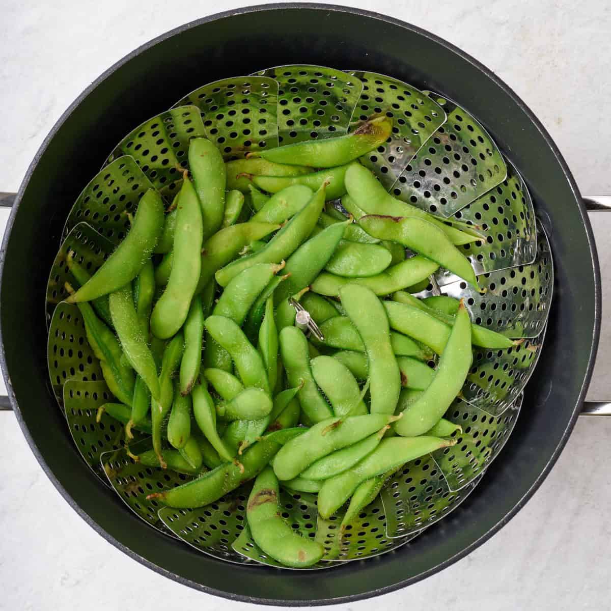 Cooked edamame in a steam basket over a pot.