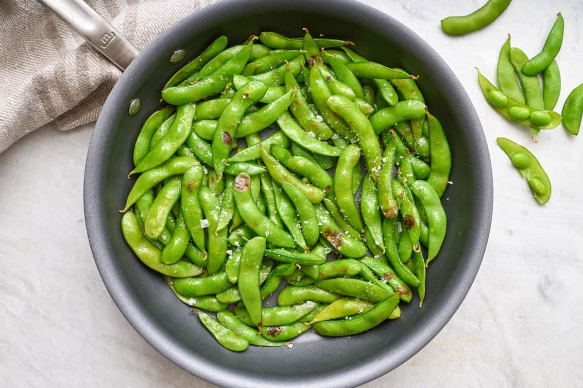 Cooked edamame in a pot with edamame spread in the background.