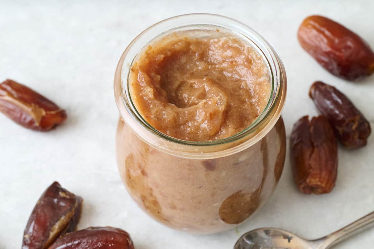 Jar of homemade date paste with whole dates and a spoon nearby.