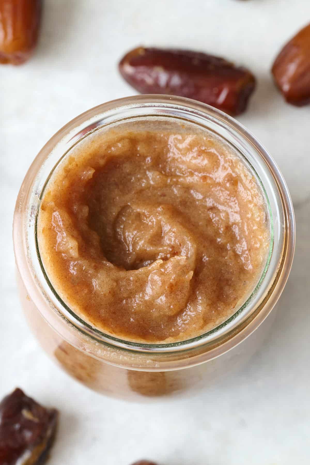 Homemade date paste in a jar with more dates nearby.