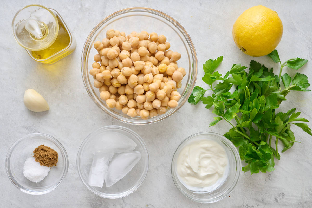 Ingredients for recipe: Chickpeas, olive oil, lemon, garlic, fresh parsley, Greek yogurt, salt, cumin, and ice cubes.