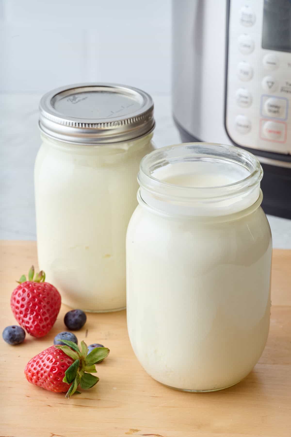 2 mason jars of yogurt with the Instant Pot and berries nearby.