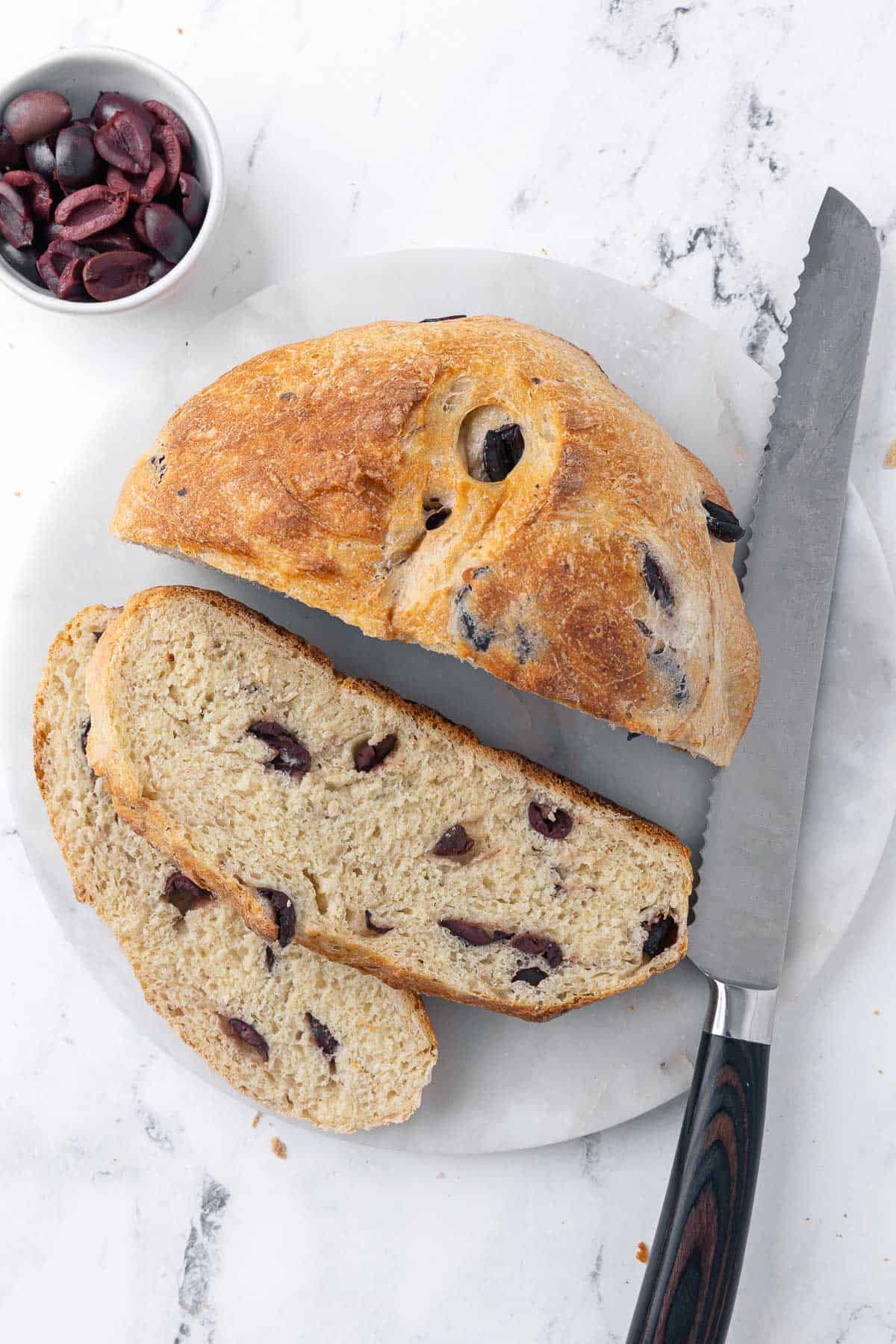 Olive bread with a few slices cut out; a bread knife and bowl of olives nearby.