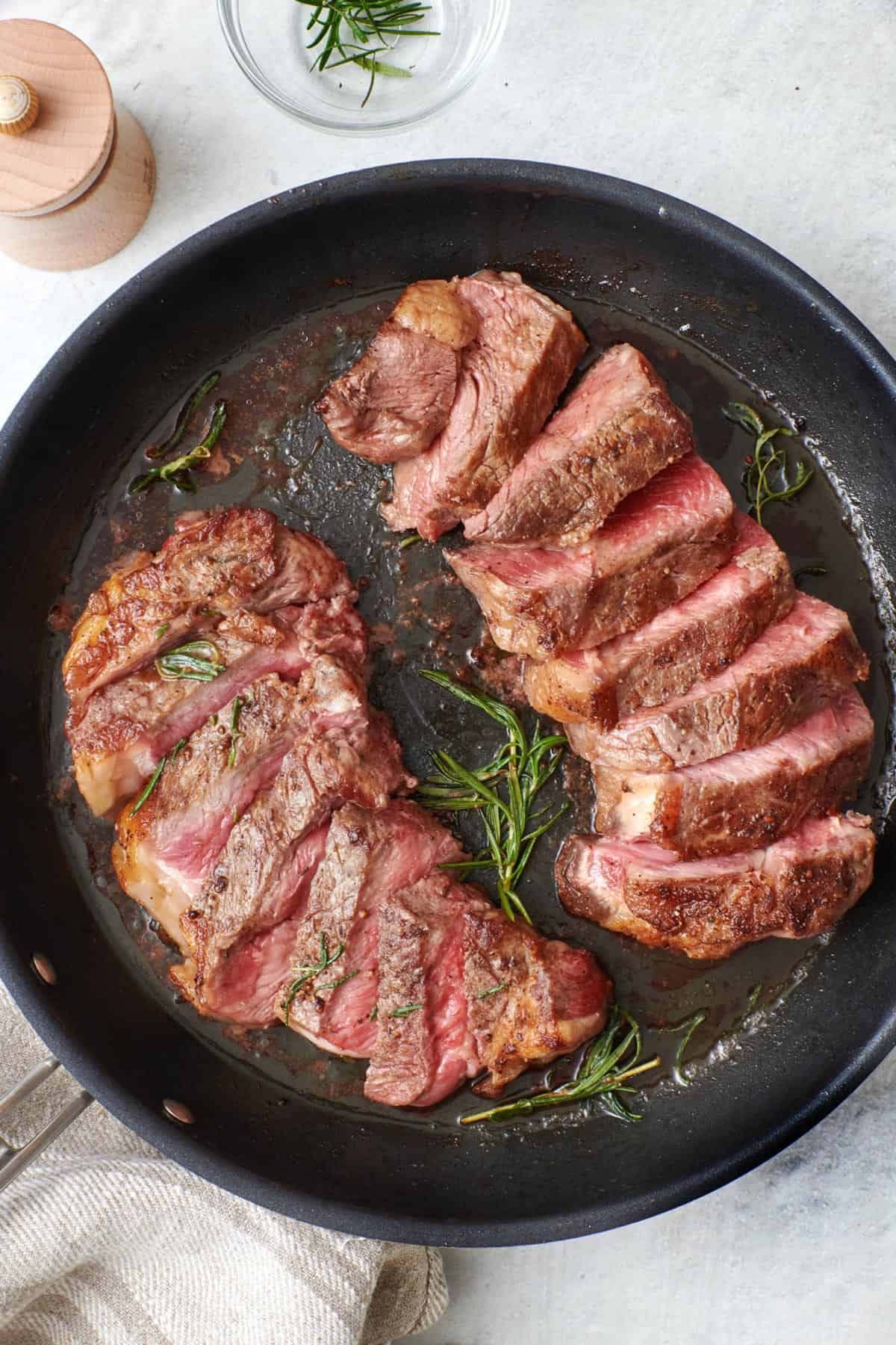 Medium-rare NY strip steaks sliced on a skillet with rosemary.