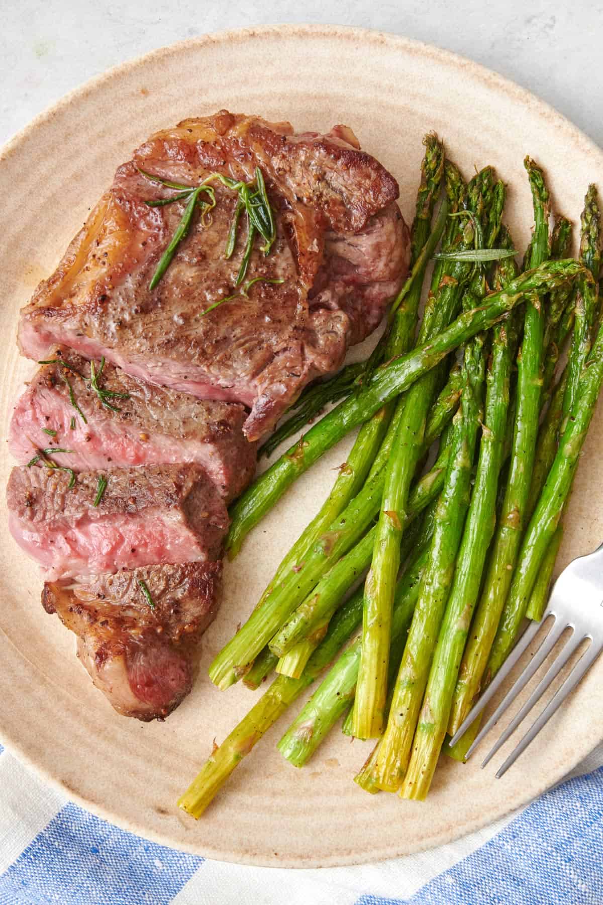 Sliced pan-seared steak on a plate with a side of cooked asparagus.